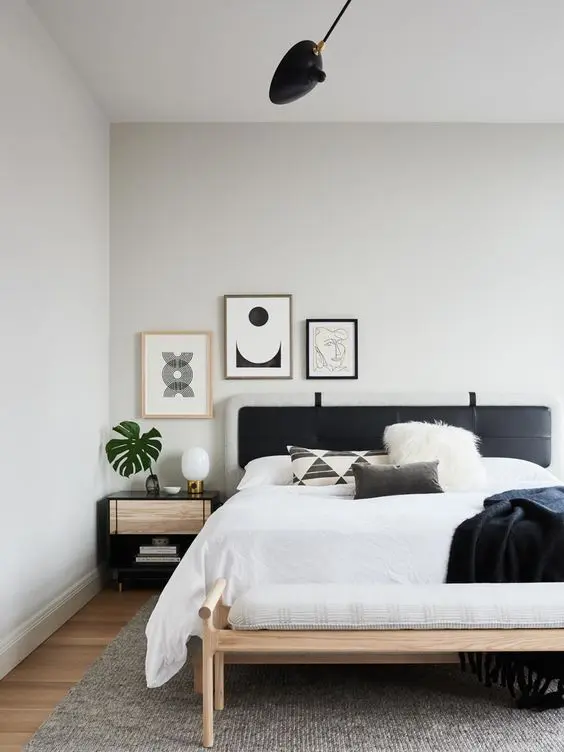 a modern boho bedroom with a bed with a black headboard, a bench, a nightstand and a small gallery wall