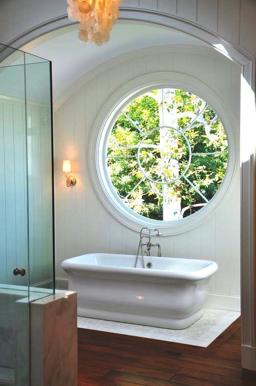 a modern farmhouse with a large porthole window next to the tub to fill the space with natural light