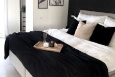 a monochromatic bedroom with a black accent wall, a bed with monochromatic bedding, a gallery wall and some decor