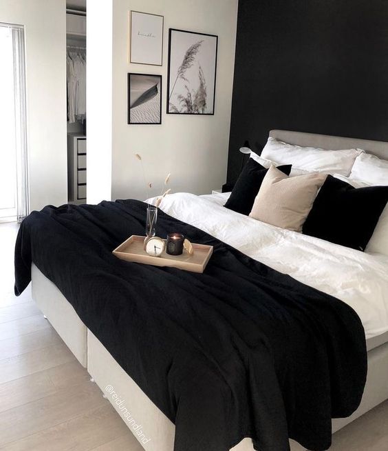 a monochromatic bedroom with a black accent wall, a bed with monochromatic bedding, a gallery wall and some decor