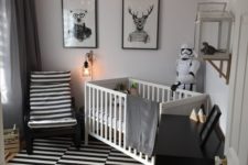 a monochromatic nursery with a striped rug and chair, a black dresser, a white crib and bulbs attached to the ceiling