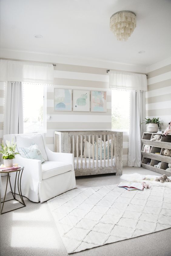 a neutral farmhouse nursery with a whitewashed crib, a unique chandelier, a printed rug and stripes on the walls