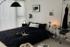 a pretty bedroom with a black bed and black bedding on the floor, a makeshift closet, a table and some artwork and pet beds