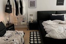 a pretty contemporary bedroom with a black bed and monochromatic bedding, a loveseat, a makeshift closet and a lamp