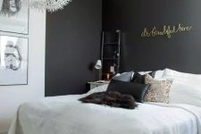 a small and lovely bedroom with black accent walls, a bed with white bedding and black pillows, a gallery wall and gold calligraphy