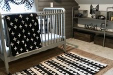 a small attic nursery with a jute rug, a printed one, a grey vintage crib, prints and a reclaimed wooden wall