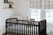 a small yet cozy nursery with plaid Roman shades, a vintage black crib, a sphere pendant lamp and floating shelves
