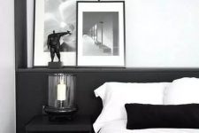 a stylish contemporary black and white bedroom with a black statement wall, a candle lantern, chic artworks and monochromatic bedding