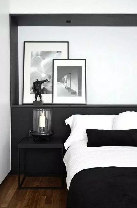 a stylish contemporary black and white bedroom with a black statement wall, a candle lantern, chic artworks and monochromatic bedding
