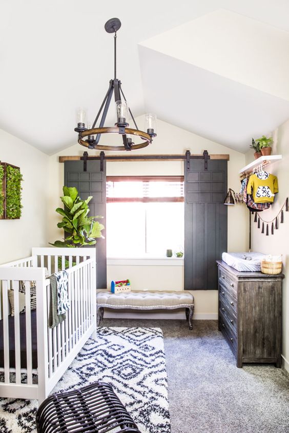 a unique farmhouse nursery with sliding shutters of vintage doors, a white crub, printed layered rugs and a vintage chandelier