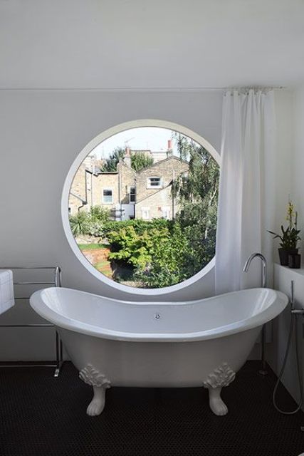 a vintage-inspired neutral bathroom with a dark floor and a large porthole window that can be covered with a curtain