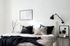 an airy Scandinavian bedroom with a white bed and contrasting bedding, a black lamp and some decor