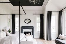 an exquisite bedroom with paneling, a black ceiling and a fireplace with a black mantel, a framed and a white loveseat