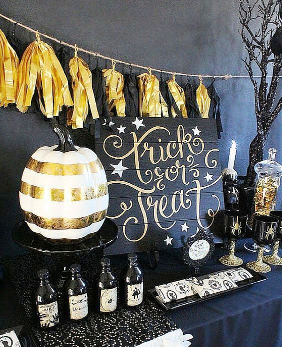 a black and gold dessert table with black and gold tassel garland, a striped pumpkin, glitter and some spider glasses