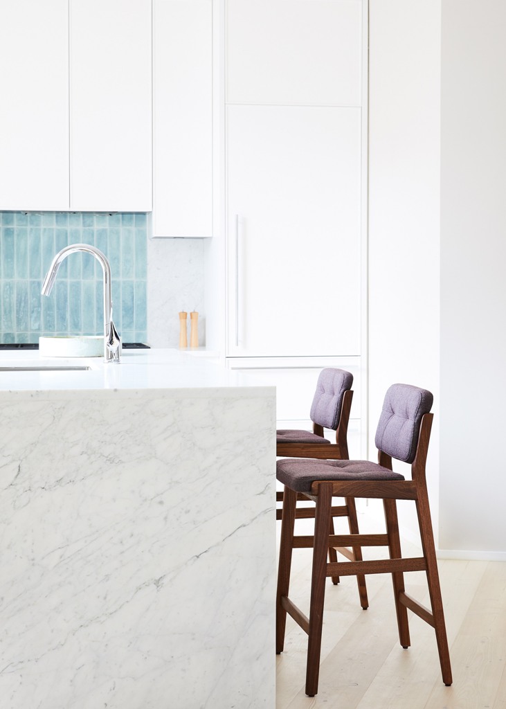 The kitchen is done with white cabinets, a white marble kitchen island and tall stools that contrast the whole space