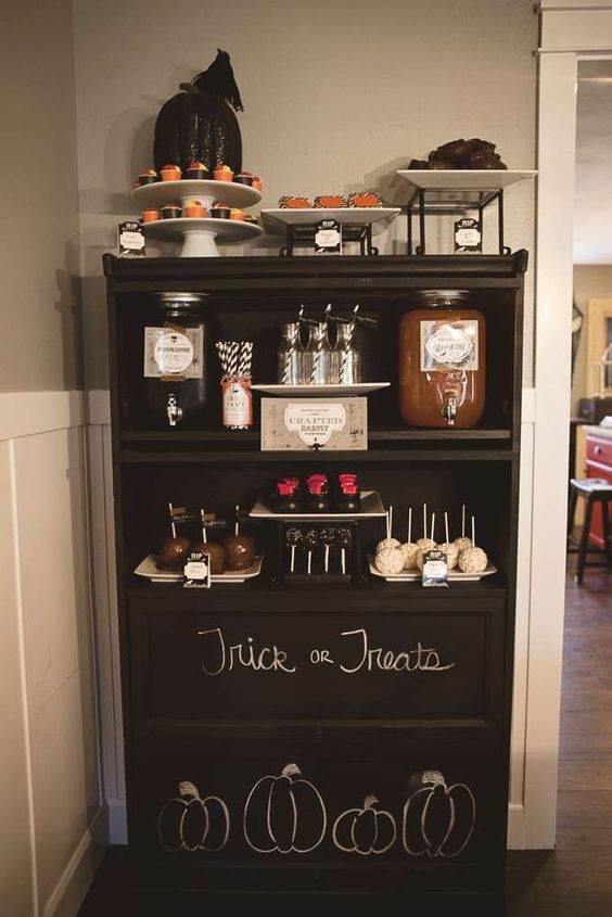 a black dessert table with chalking, blackbirds, a sparkling black pumpkin and lots of food and drinks