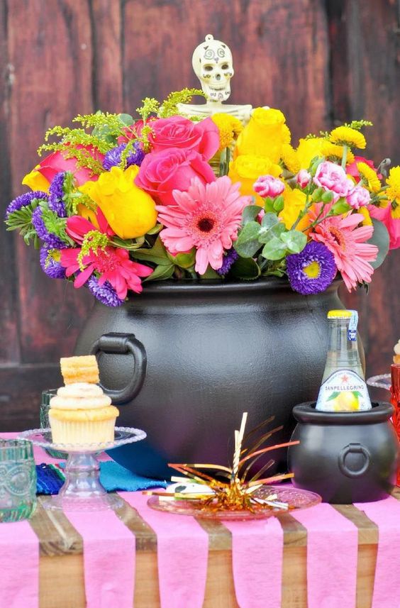 a bright Halloween centerpiece of a black cauldro, bright blooms in pink, purple and yellow plus a skeleton