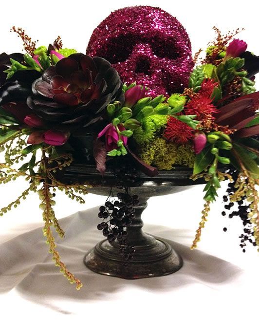 a black bowl with succulents, cascading greenery and branches, dark blooms and a sprakling red skull