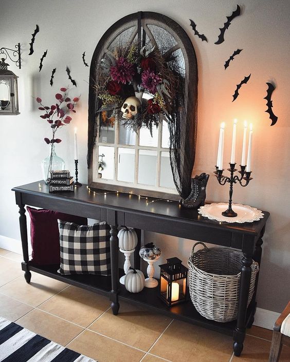 a Halloween entryway console with pumpkins, bats on the wall and a darkflorla wreath with a skull for a moody touch