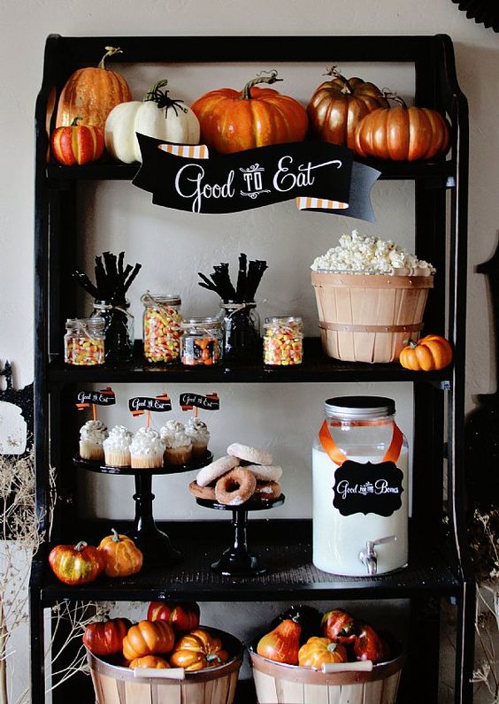 a dessert buffet with pumpkins in a basket, painted pumpkins on the upper shelf and some treats that match