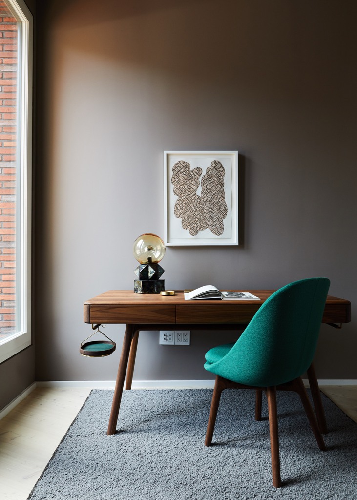 The cozy home office nook is furnished with a stylish sleek desk, an upholstered chair and a catchy table lamp