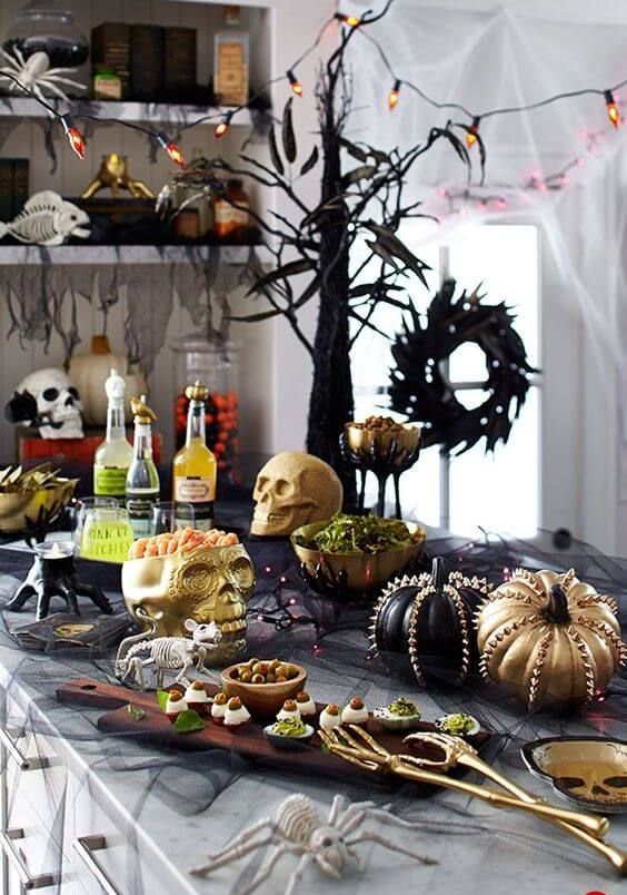 a stylish Halloween food station with skulls, lights, studded pumpkins, spiders and skeletons plus tasty food