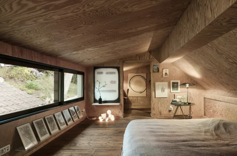 The master bedroom is designed like a cabin and is all clad with light-colored plywood, there some lights, art and a work space