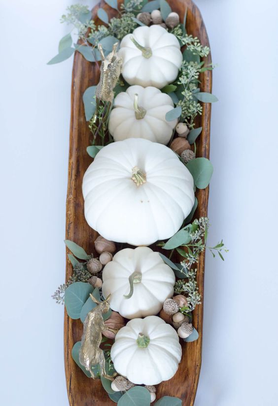 a fall centerpiece of a wooden bowl, acorns, greenery and white pumpkins - everything natural here