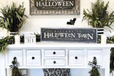 10 a simple and fresh Halloween entryway console with black and white pillows, greenery arrangements, signs and candles is chic