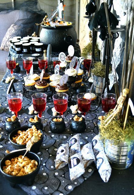 a stylish Halloween buffet with little black cauldrons for food, red bloody drinks, a large cauldron with bottles and skeletons