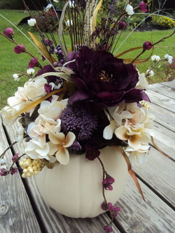 a white pumpkin centerpiece with neutral and deep purple flowers, berries and branches for Halloween