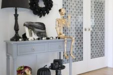 11 an entryway console decorated with a giant skull, a gold skeleton, black and white pumpkins, a black wreath and tulle
