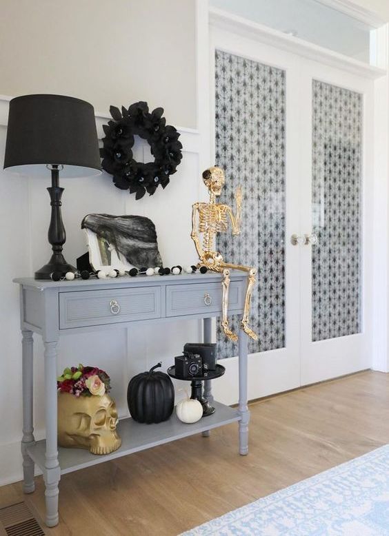 An entryway console decorated with a giant skull, a gold skeleton, black and white pumpkins, a black wreath and tulle