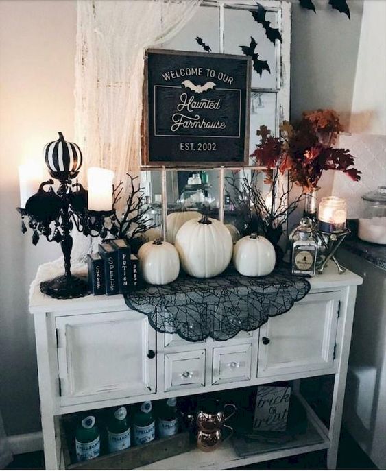 A white entryway console with white pumpkins, black lace, black and white pumpkins, candles and a fall leaf arrangement