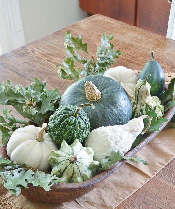 a dough bowl with pumpkins, gourds and freen leaves will make up an amazing fall centerpiece