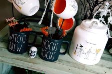 14 a drink station with cool Halloween mugs, a pumpkin with straws, a skeleton and some branches and Halloween pumpkins