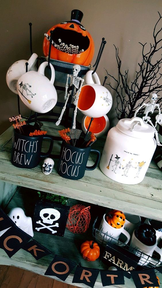 a drink station with cool Halloween mugs, a pumpkin with straws, a skeleton and some branches and Halloween pumpkins