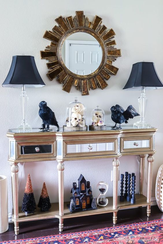 A refined entryway console with black lamps, blackbirds, black candleholders, a black house and Halloween trees