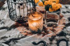 14 stylish Halloween coffee table decor with a splatted tablecloth, a cage with a plush, a candleholder and bold blooms in a vase