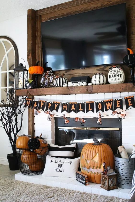 a bold Halloween mantel with a bunting, fake pumpkins including carved ones, decorated and lettered ones, lanterns and a spooky tree