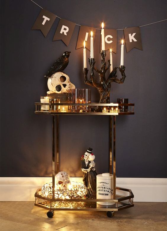 a glam Halloween bar cart with candles, lights, skulls, figurines and a bunting - just add some drinks and voila