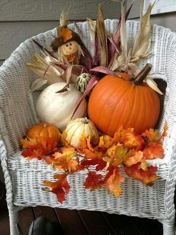 a white chair decorated with fall leaves, pumpkins, corn husks and some greenery will spruce up your home or porch