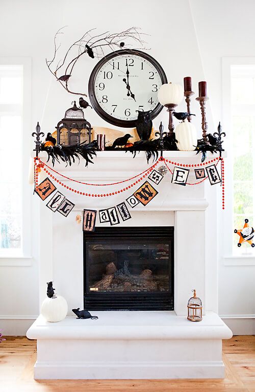 a bold Halloween mantel with a colorful bunting, blackbirds, feathers, a cage, candles and pumpkins