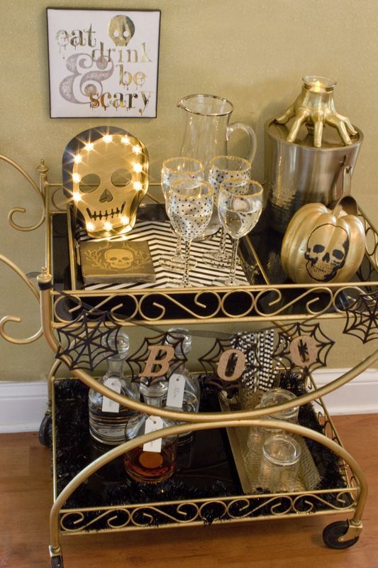 a gorgeous black and gold Halloween bar cart with skeletons, striped mats, a garland with spiderwebs and a hand candleholder