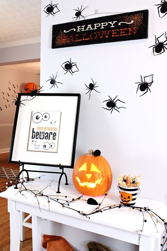 a Halloween entryway console with a Jack-o-lantern, a sign, some spiders and art and a creepy branch