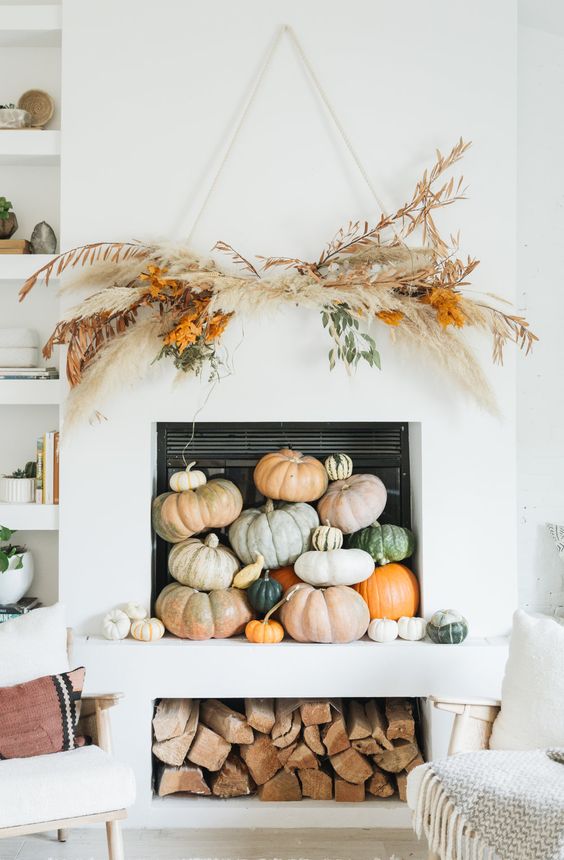 a beautifully styled fireplace with natural pumpkins, dried grass. leaves and branches