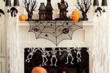 17 a bright Halloween mantel with carved pumpkins, skeletons, a piderweb, haunted houses and a banner over it