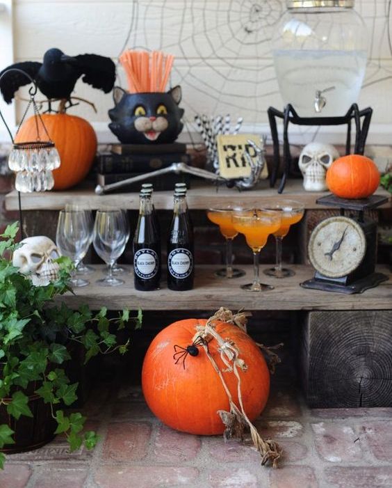 a Halloween drink bar with a pumpkin, skulls, blackbirds, spiderweb, greenery and skeleton hands