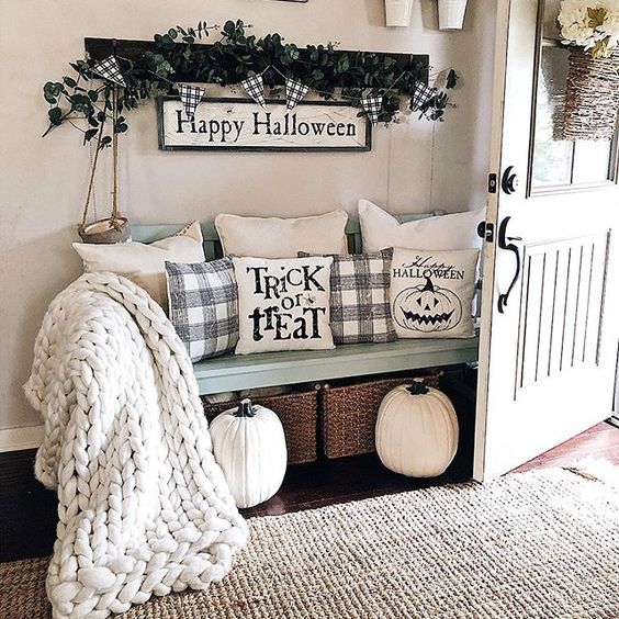 A farmhouse entryway dressed up for Halloween with Halloween pillows, a sign and some dark greenery