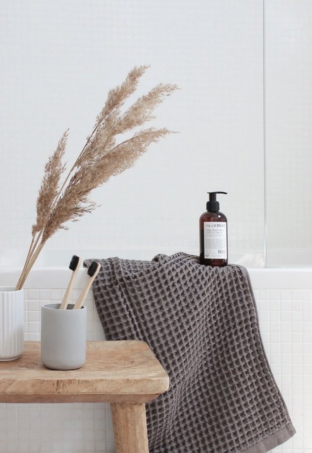 a grey towel and a dried grass arrangement and a plywood stool make the bathroom feel like fall